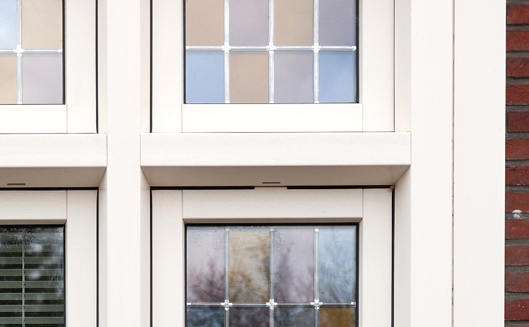Nahaufnahme eines weißen Sprossenfensters mit strukturiertem Glas, eingebettet in eine moderne Fassade.